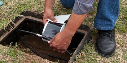 Electrician crouching over and taping a slice for a subterranean cable with electrical tape.
