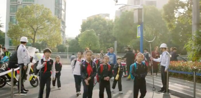 Group of young Chinese students crossing a busy street with the help of school patrol volunteers.
