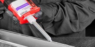 Profissional utilizando aplicador para dispenser de cola estrutural 3M, aplicando adesivo em uma peça metálica.
