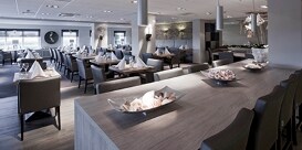 Um restaurante cheio de mesas prontas tem acabamentos atraentes em suas bancadas e pisos.
