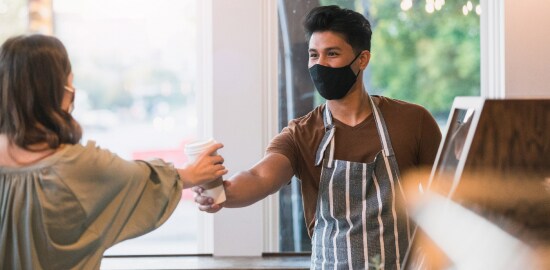 Um trabalhador entrega uma bebida a uma cliente em um restaurante.
