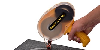 A worker applies tape using a tape gun that applies the tape and removes the liner at the same time
