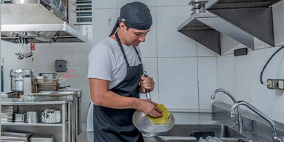 Um funcionário lavando louças em uma cozinha comercial.

