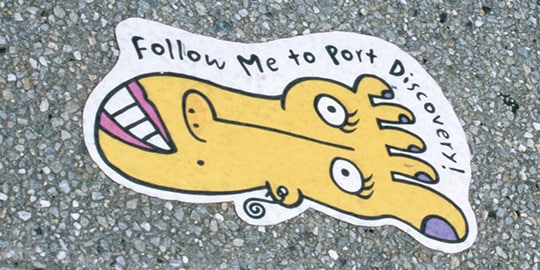 Uma calçada com um gráfico de vinil com o desenho de um pé com um rosto e algumas palavras.
