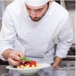 Um chef adiciona cuidadosamente um toque final a um prato de massa.