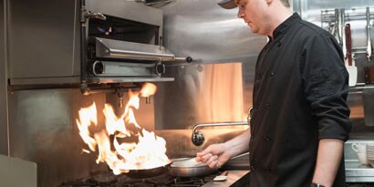 Um funcionário de restaurante cozinha com uma frigideira em chamas.
