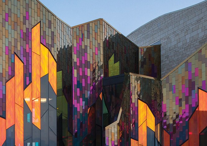 Imagem externa de edifício com painéis de janelas angulares cobertos com acabamento para vidro 3M Dichroic em tons quentes.