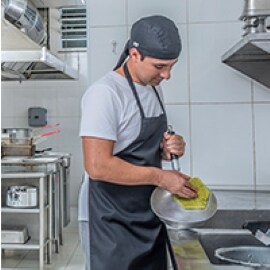 Um trabalhador de cozinha comercial esfrega uma panela em uma pia.