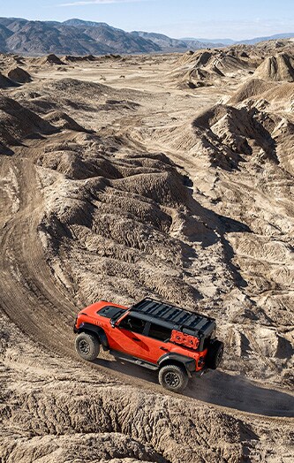 SUV com Película para Envelopamento vermelha dirigindo em um caminho off-road acidentado no deserto com montanhas no horizonte.
