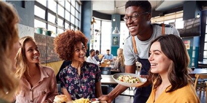 Um garçom traz a comida para quatro clientes sorridentes.
