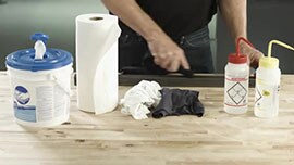 Video still showing cleaning supplies: disposable towels, cloth wipes and bottles of acetone and isopropyl alcohol