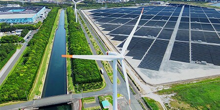 Imagem aérea de uma fazenda solar e uma torre eólica.
