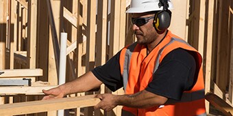 Worker at construction site wearing safety eyewear, hardhat, safety vest and hearing protection
