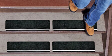 Pessoa descendo um lance de escadas com fitas antiderrapantes 3M aplicadas.
