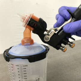 Mão usando luvas segurando uma pistola de pulverização conectada a um copo PPS para aplicação de pintura.
