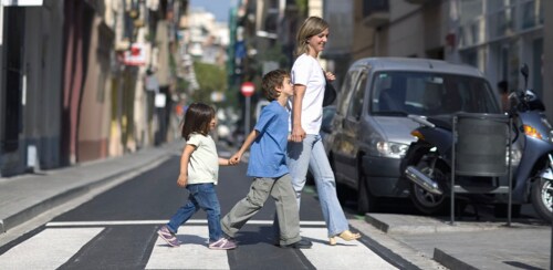 Mother with young son and daughter holding hands crossing a crosswalk in the city.
