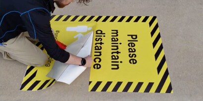 Trabalhador da 3M colocando um  gráfico quadrado em uma calçada de concreto.

