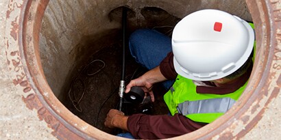 Electrician in a manhole repairing wire with electrical tape.
