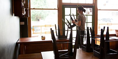 Umfuncionário de restaurante empilhando bancos em cima de uma mesa vazia.
