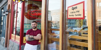 Um proprietário de restaurante em pé do lado de fora de seu restaurante.
