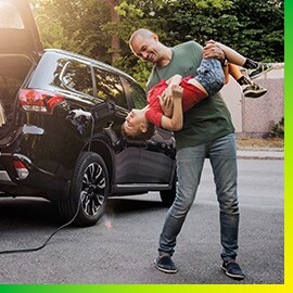 Homem brincando com seu filho ao lado de um carro preto carregando na garagem.