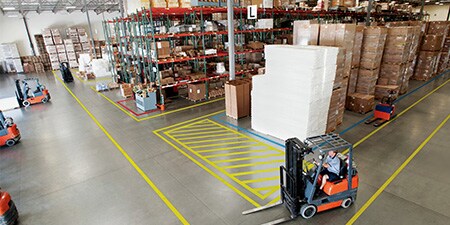 Demarcação de segurança impressa e personalizada da 3M aplicada ao chão, lembrando as pessoas de ficarem a 2 metros de distância.

