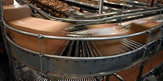 Imagem de caixas desfocadas se movendo rapidamente em uma curva em uma esteira transportadora.
