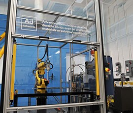Image of a robot in a glass cage used to demonstrate automated application of adhesives