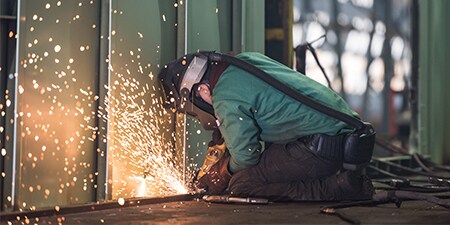 welder grding and wearing a welding hood with papr
