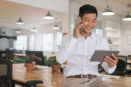 Imagem de homem de negócios sorridente falando ao telefone e olhando para um tablet.
