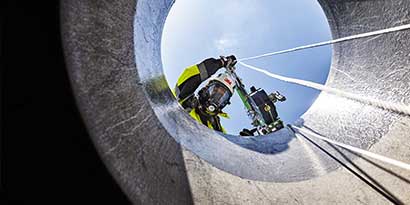 Worker using confined space access equipment looking down a confined space access portal
