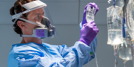 Clinician wearing a half facepiece resuable respirator and faceshield checking an IV
