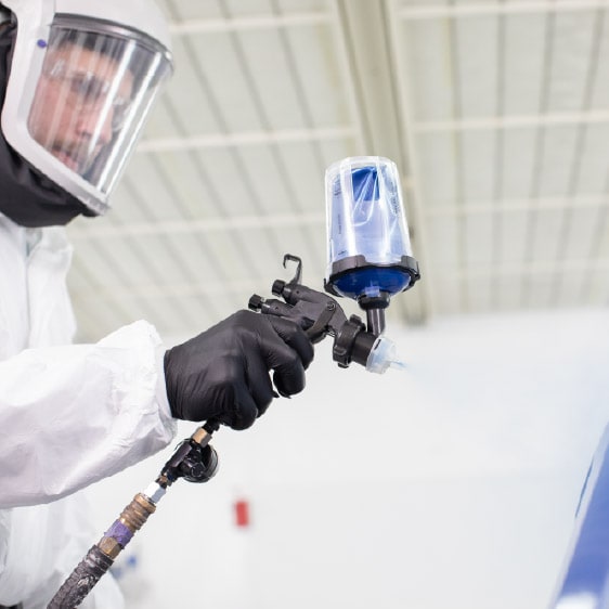 Mão com luva posicionando um disco de lixa roxo em uma lixadeira orbital, com faíscas ao fundo em um ambiente de oficina.
