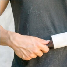 Pessoa passando rolo removedor de fiapos em camiseta escura para remover pelos.
