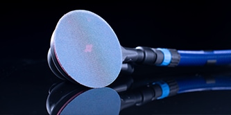 Close de uma lixadeira com um disco abrasivo azul, mostrada contra uma superfície escura e reflexiva.
