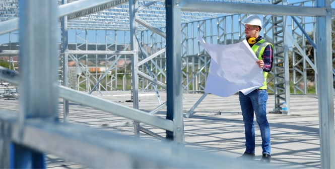 Dois trabalhadores com coletes de alta visibilidade e capacetes estão em uma instalação industrial iluminada, cercados por grandes tubulações, válvulas e equipamentos de processamento.