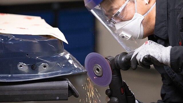 Operário utilizando um disco abrasivo 3M no metal enquanto usa um equipamento de proteção individual.
