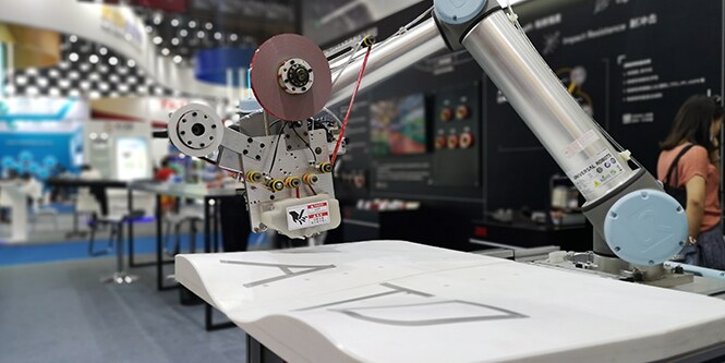 Image of a robot arm with applicator head poised over a workpiece of variable vertical depth
