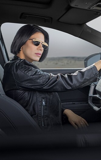 Mulher sentada em carro no banco do motorista com óculos de sol.
