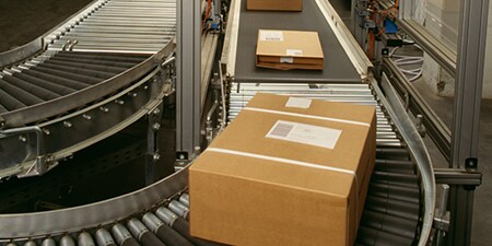 Três pacotes prontos para envio em uma esteira transportadora.
