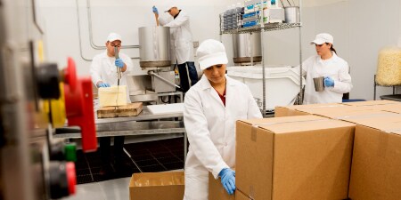 A worker in an industrial kitchen setting places a sealed box next to other similar boxes
