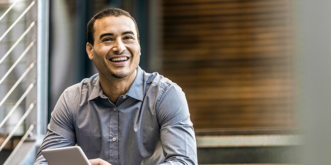 Male, young professional sitting on stairs holding small tablet.
