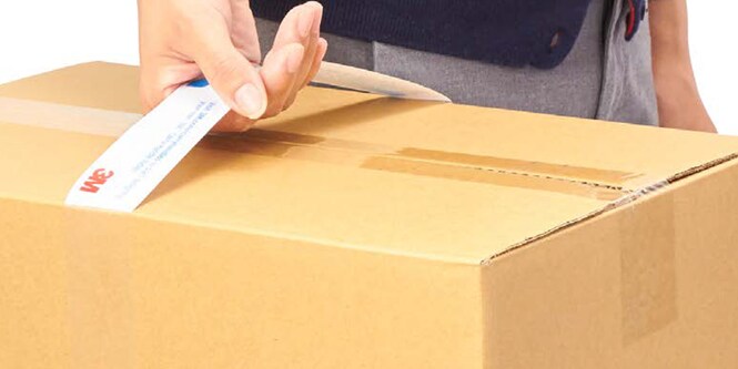 Um close-up da mão de uma pessoa segurando uma caixa de papelão por uma alça.
