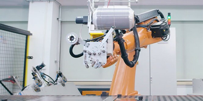 Image of a robot arm with applicator head holding a wide roll of level-wound tape
