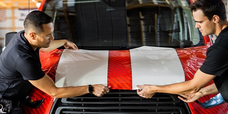 Dois instaladores posicionando filme IJ280 no capô.
