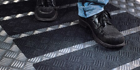 Alguém andando sobre fitas antiderrapantes 3M Safety-Walk aplicadas em um piso.
