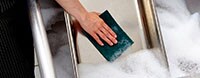 A restaurant worker in a commercial kitchen scours a large pan in soapy water.