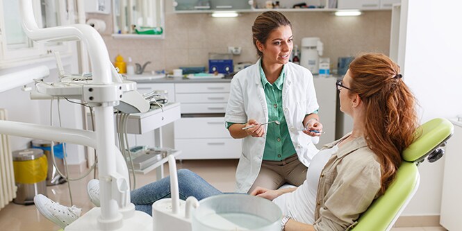 Female clinician speaking to female patient in dentist chair
