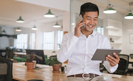 Imagem de homem de negócios sorridente falando ao telefone e olhando para um tablet.
