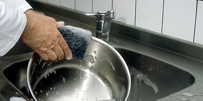 Imagem de uma pessoa lavando uma panela de metal.